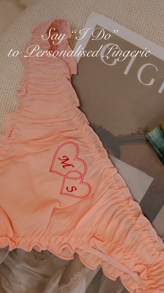 A close-up aesthetic shot of ruffled, personalized lingerie featuring embroidered initials on heart-shaped patches, evoking a romantic bridal mood.